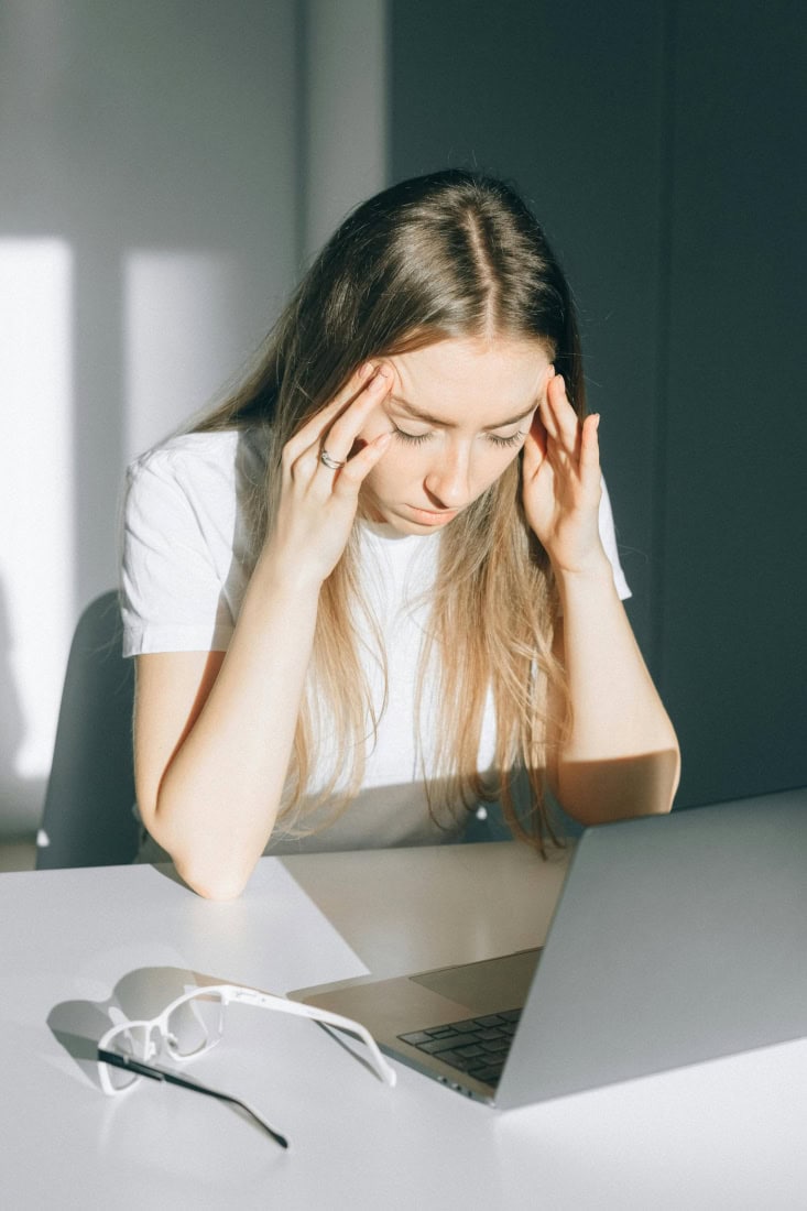 Hoofdpijn ervaren door stress of vermoeidheid, vrouw met pijnlijke hoofdpijn aan tafel.