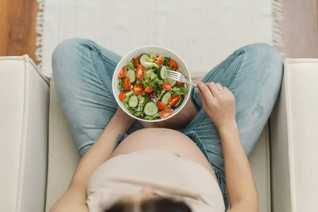 Gezonde salade met groenten en een zwangere vrouw eet gezond voeding.